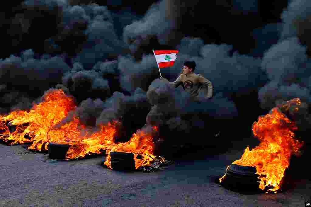 An anti-government demonstrator jumps over tires set on fire to block a main highway during a protest in the town of Jal el-Dib, north of Beirut, Lebanon.