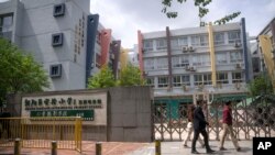 Gente pasa frente a una escuela primaria cerrada en Beijing, 28 de abril de 2022. Mientras otros países eliminan restricciones y algunos funcionarios dicen que lo peor ha pasado, China mantiene cerradas las fronteras y permite apenas los desplazamientos esenciales.