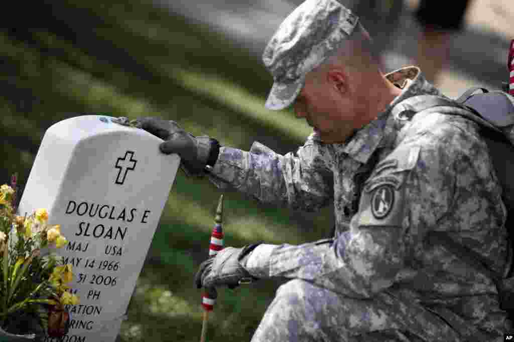 A member of the U.S. Army Old Guard pays his respects at the grave of U.S. Army Major Douglas Sloan, before placing a flag at one of the over 220,000 graves of fallen U.S. military service members buried at Arlington National Cemetery.