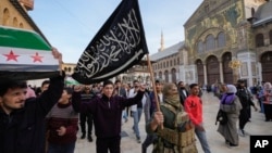 FILE - A masked opposition fighter carries a flag of Hayat Tahrir al-Sham in the courtyard of the Umayyad Mosque in the old walled city of Damascus, Syria, Dec. 10, 2024.