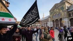 FILE - A masked opposition fighter carries a flag of Hayat Tahrir al-Sham in the courtyard of the Umayyad Mosque in the old walled city of Damascus, Syria, Dec. 10, 2024.