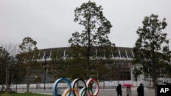 People walk past the Olympic rings near the New National Stadium in Tokyo, March 4, 2020. 