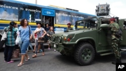 Thai soldiers stand guard near their vehicle as bus passengers walk past in Bangkok's Victory Monument, Thailand, June 8, 2014.