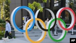 Seorang perempuan dan anjingnya berjalan melewati ring Olimpiade di Tokyo, 20 April 2021. (Foto AP / Koji Sasahara)