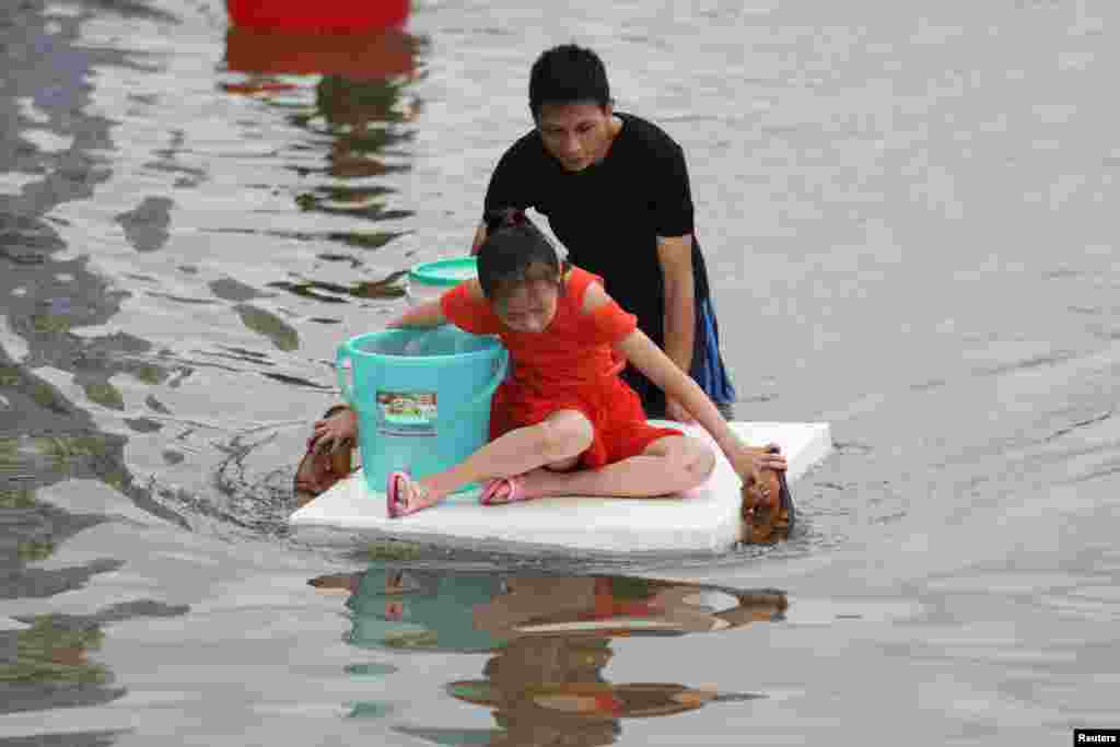 A girl, floating on a foam board, paddles with slippers as a man pushes the board through a flooded street, following heavy rainfall at a town in Shantou, Guangdong province, China, Sept. 2, 2018.