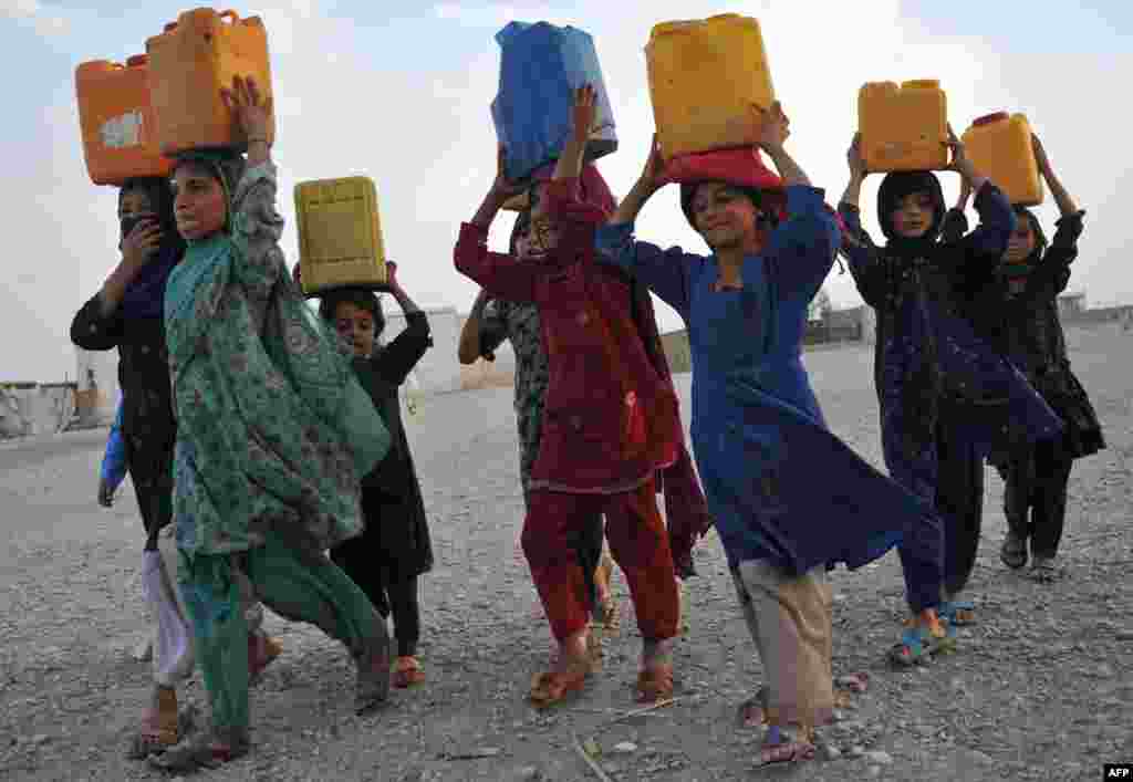 Internally displaced Afghan refugee children carry water in plastic bottles after being filled at a communal pump in Rodat district of Nangarhar province, Afghanistan.