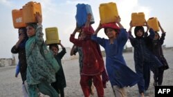 Internally displaced Afghan refugee children carry water in plastic bottles after being filled at a communal pump.