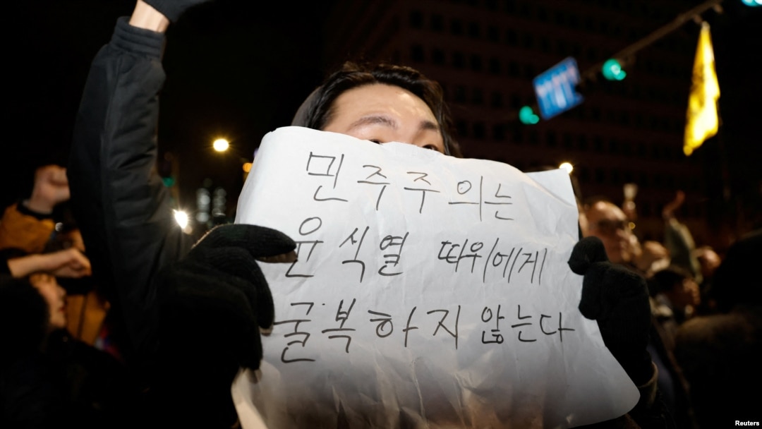 A person holds a placard that reads "Democracy will not surrender to Yoon Suk Yeol" as people gather outside the National Assembly, after South Korean President Yoon Suk Yeol declared martial law, in Seoul, South Korea, Dec. 4, 2024. 