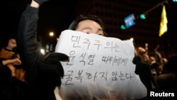 A person holds a placard that reads "Democracy will not surrender to Yoon Suk Yeol" as people gather outside the National Assembly, after South Korean President Yoon Suk Yeol declared martial law, in Seoul, South Korea, Dec. 4, 2024. 