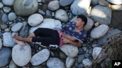 Un hombre que forma parte de una caravana de migrantes, duerme en un lecho de rocas a orillas del río Huixtla, estado de Chiapas, México, el martes 26 de octubre de 2021, en un día de descanso antes de continuar su caminata por el sur de México. a la frontera de Estados Unidos.