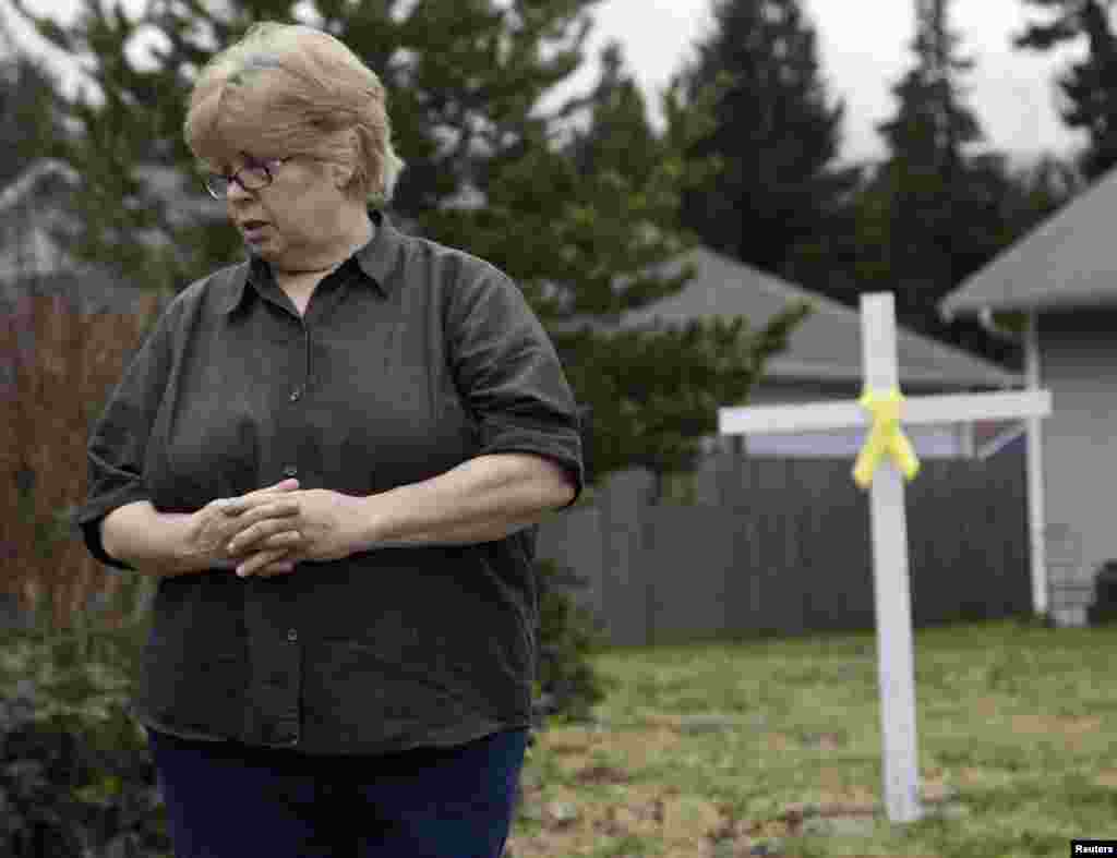 Brenda Moe looks on after placing a cross with a yellow ribbon for victims of the Oso, Washington mudslide on her front lawn in Darrington, Washington, March 27, 2014. 