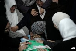 FILE - Palestinian women gather around the body of Muhammad Jalamneh, draped in the Hamas militant group flag, in the morgue of Ibn Sina Hospital after he was killed in an Israeli military raid in the West Bank town of Jenin, January 30, 2024.