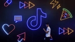 Seorang pria memegang ponsel berjalan melewati logo Tiktok milik perusahaan China ByteDance di sebuah pameran di Hangzhou, Provinsi Zhejiang, 18 Oktober 2019. (Foto: Reuters)