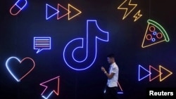 Seorang pria memegang ponsel berjalan melewati logo Tiktok milik perusahaan China ByteDance di sebuah pameran di Hangzhou, Provinsi Zhejiang, 18 Oktober 2019. (Foto: Reuters)