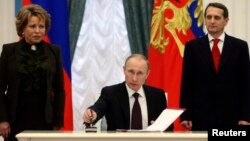 Russian President Vladimir Putin signs legislation completing the process of absorbing Crimea into Russia during a Kremlin ceremony in Moscow on March 21, 2014. 