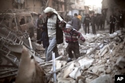 FILE - A man walks with a pair of children in hand through the rubble in Eastern Ghouta, Syria, Dec. 24, 2015.