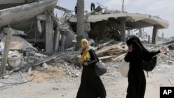 Dua orang perempuan Palestina berjalan di antara reruntuhan di Gaza, sementara gencatan senjata 72 jam bertahan di sana (6/8).