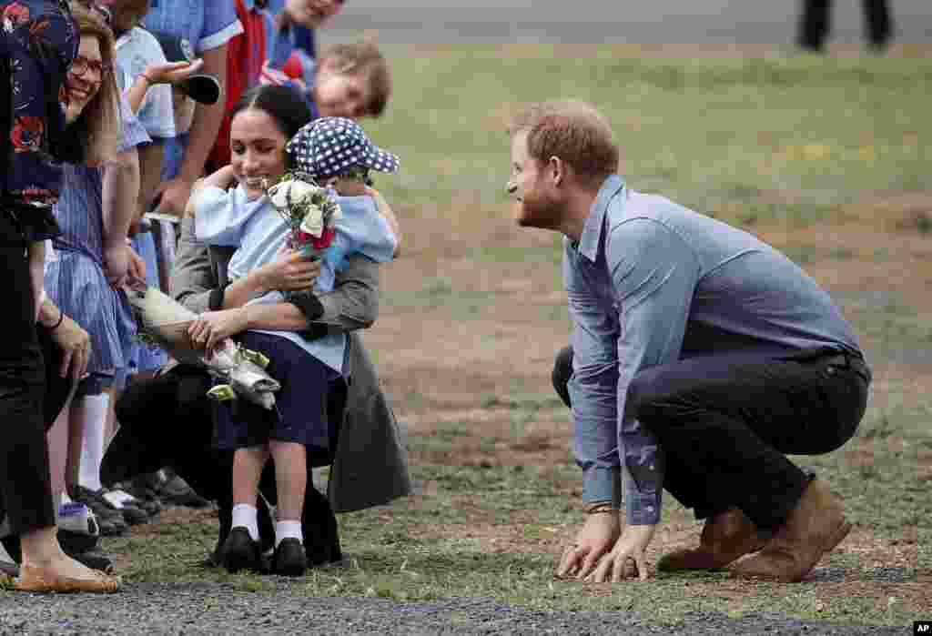Britain&#39;s Prince Harry looks on as his wife Meghan, Duchess of Sussex, is hugged by Luke Vincent, 5, on their arrival in Dubbo, Australia.