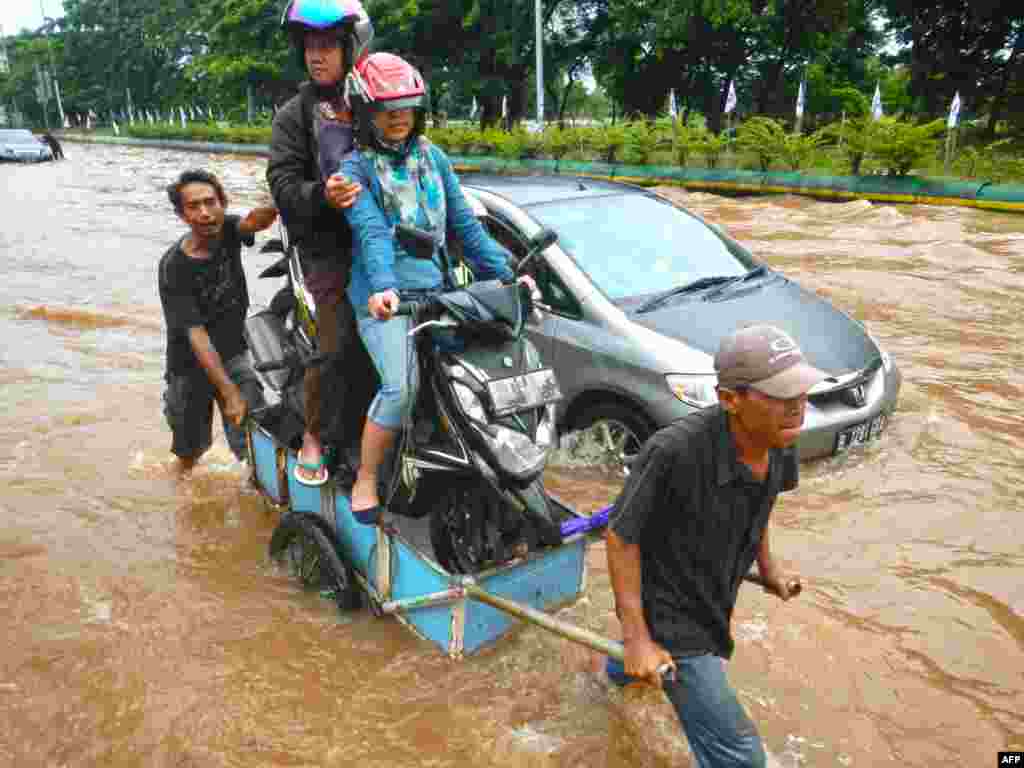 Người dân vượt qua một đoạn đường bị ngập lụt ở Jakarta. Mưa gió mùa lớn đã làm ngập lụt nhiều đoạn đường ở thủ đô Indonesia, khiến người lưu thông bị mắc kẹt.