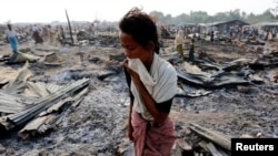 A woman walks among debris after fire destroyed shelters at a camp for internally displaced Rohingya Muslims in the western Rakhine State near Sittwe, Myanmar. 