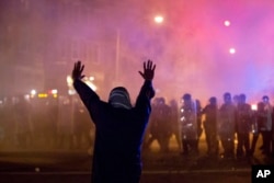 FILE - A protester faces police enforcing a curfew in Baltimore, April 28, 2015, .