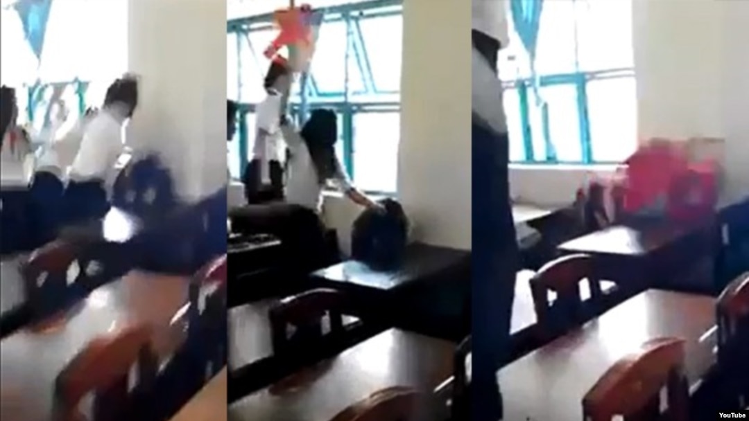 Nhóm nữ sinh dùng ghế nhựa phang liên tiếp vào đầu, đấm túi bụi, kéo và giật tóc một nữ sinh cùng lớp (ngồi) trong khi các em khác đứng xem. (Ảnh từ clip trên YouTube).