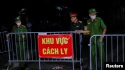 Policías junto a soldados del ejército remueven una barrera de metal que señalizaba una zona en cuarentena por COVID-19 a las afueras de Hanoi, la capital de Vietnam.