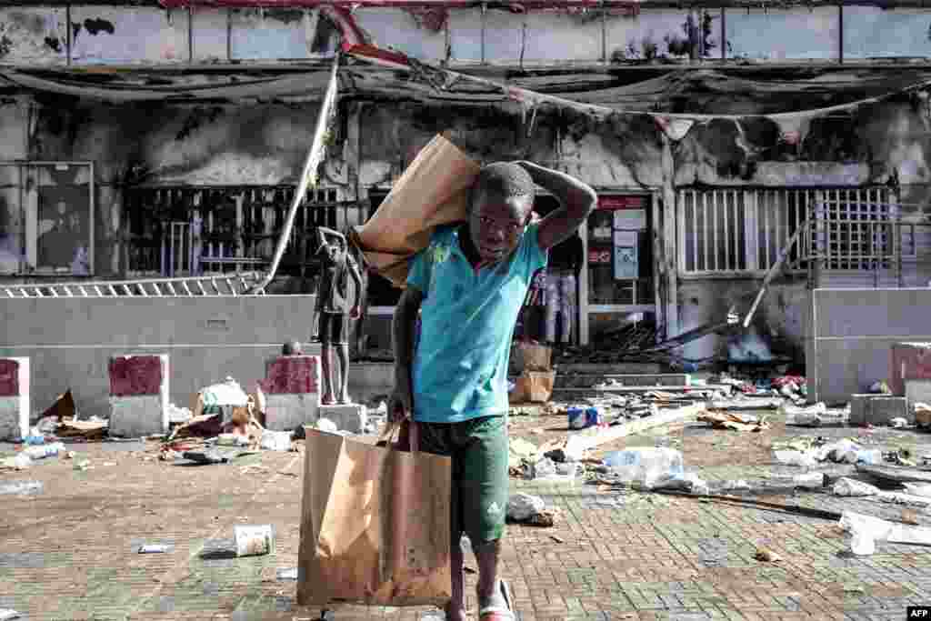 A boy walks away with grocery bags from a burnt down and looted Auchan supermarket in the up-market area of Almadies in Dakar, March 6, 2021, as protests have been ongoing for three days in Senegal after opposition leader Ousmane Sonko was arrested following rape charges.