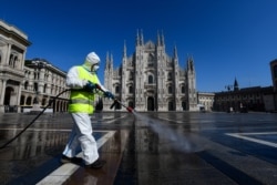 FILE - An employee sprays disinfectant on Piazza Duomo in Milan during Italy's lockdown aimed at curbing the spread of the COVID-19 infection, March 31, 2020.