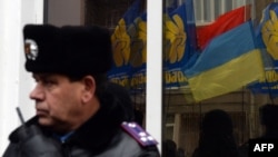 A Ukrainian police officer stands by as the flags of radical party Svoboda (Freedom) are reflected in the window during a protest against political repression in front of the Ukrainian Interior Ministry headquarters in Kiyv, Nov. 28, 2013.