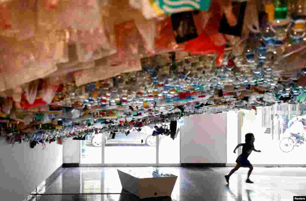 A girl runs during an exhibition of a hanging art installation made from scraps of plastic bags, bottles, cans and containers, entitled &#39;Reduce&#39;, at the French Cultural Center in Hanoi, Vietnam.