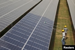 FILE - Workers clean photovoltaic panels at a solar power plant in Gujarat, India, July 2, 2015.