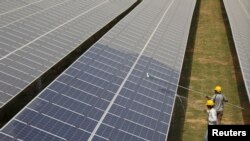 FILE - Workers clean photovoltaic panels at a solar power plant in Gujarat, India, July 2, 2015. 