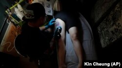 In this Wednesday, Oct. 23, 2019, photo, tattoo artist Mike Chan applies ink to the leg of a client who goes by the single name "Mary" in Hong Kong.