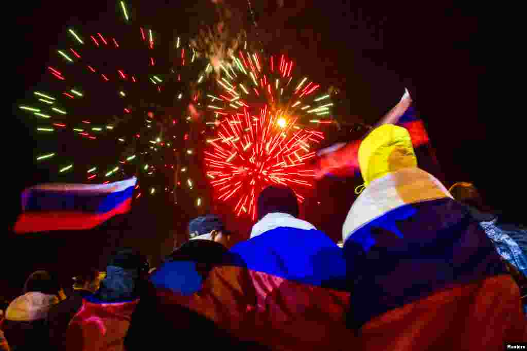 People wrapped with Russian flags watch fireworks during celebrations after the preliminary referendum results were announced in Lenin Square in the Crimean capital Simferopol, March 16, 2014. 