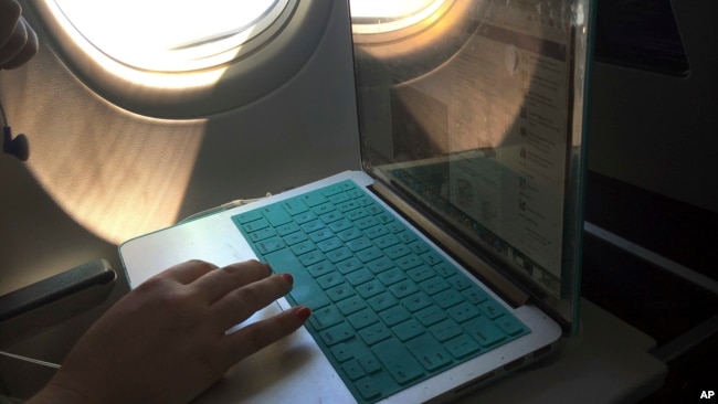 FILE - A passenger uses a laptop aboard a commercial airline flight from Boston to Atlanta, July 1, 2017. The airline industry is warning that thousands of flights could be grounded or delayed if the 5G rollout takes place near major airports.