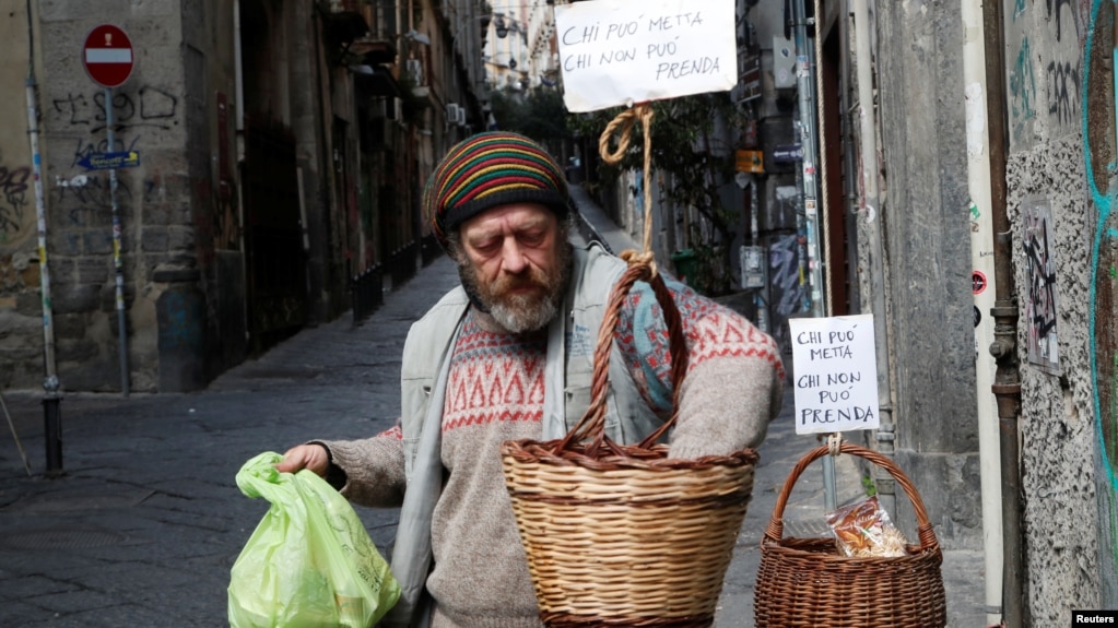A man takes products from a basket, that were hung up so people can donate or take for free food, as Italy struggles to contain the spread of coronavirus disease (COVID-19), in Naples, Italy March 30, 2020. (REUTERS/Ciro De Luca)