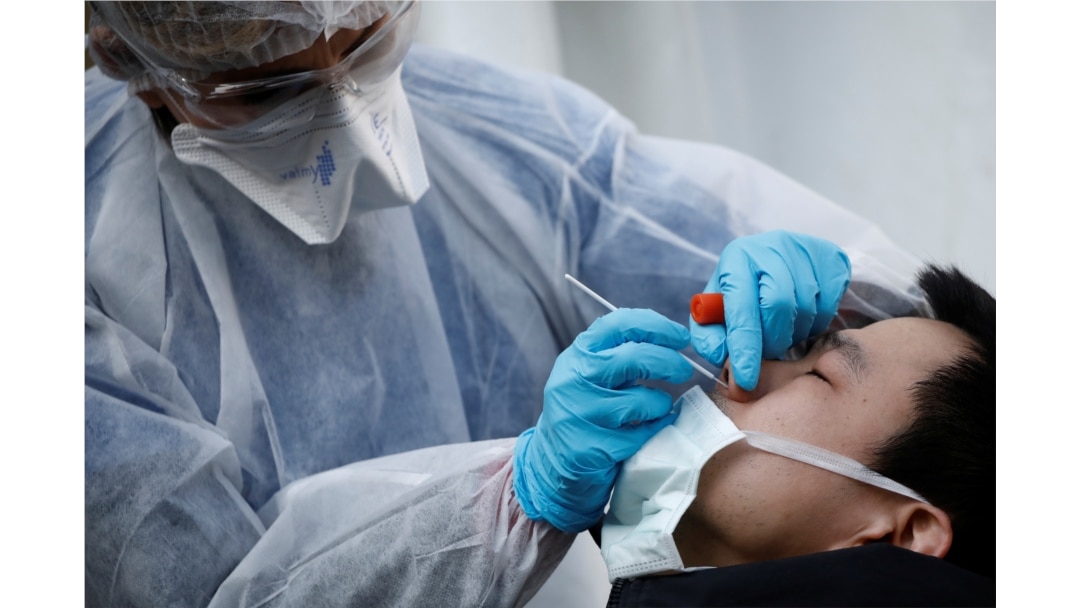 A medical biologist, wearing a protective suit, administers a nasal swab to a patient at a drive-through testing site for coronavirus disease (COVID-19) at the city hall of the 17th district in Paris