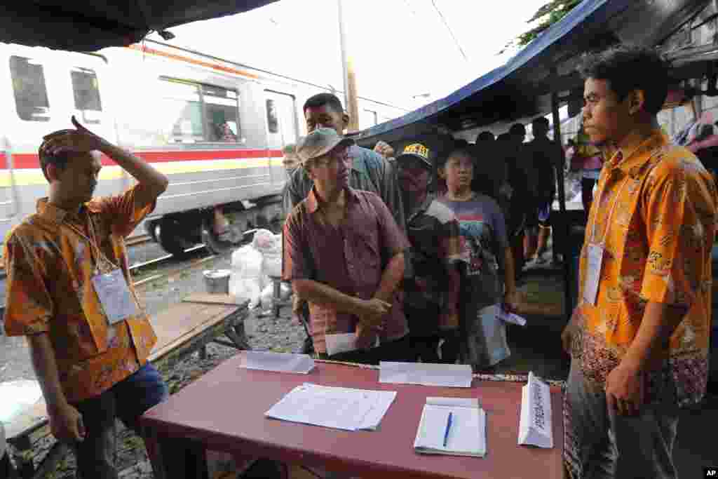 Warga antre untuk melaksanakan hak pilih di sebuah TPS yang didirikan di sebelah jalur kereta api di Jakarta, Rabu (17 April 2019). (Foto: Tatan Syuflana/AP)