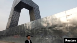 FILE - A man walks outside a construction site, next to the China Central Television (CCTV) building in Beijing's central business district. 