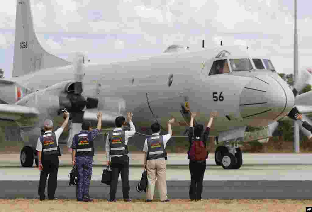 Members of Japan's disaster relief team wave to a Japan Maritime Self-Defense Force aircraft as it prepares to to search for flight MH370, at the Royal Australian Air Force Base Pearce in Perth, March 24, 2014.
