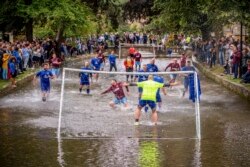 Pesepakbola Bourton Rovers berebut bola di Sungai Windrush dalam pertandingan sepak bola tradisional tahunan di desa Cotswolds, Bourton-in-the-Water, Inggris, Senin, 30 Agustus 2021. (Ben Birchall/PA via AP)