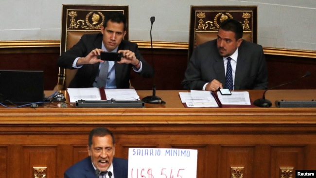 El diputado y economista Jose Guerra sostiene un cartel con el equivalente del salario mínimo en Venezuela, Bs. 18.000, en dólares, unos $5.45. "El más bajo del mundo", señaló durante una sesión del parlamento. Foto: Reuters.