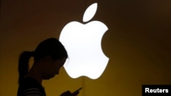 FILE - A woman looks at the screen of her mobile phone in front of an Apple store in Shanghai, China.