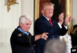 President Donald Trump applauds as retired Army medic Jim McCloughan points to his family after bestowing the nation's highest military honor, the Medal of Honor, to McCloughan, during a ceremony in the East Room of the White House, July 31, 2017.