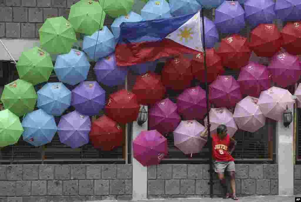 A Filipino stands beside the Philippine flag as colorful umbrellas adorn a village hall in suburban San Juan, east of Manila, Philippines.