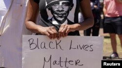 Seorang perempuan mengenakan kaus bergambar mantan presiden AS Barack Obama sambil memegang poster dalam unjuk rasa memprotes kematian pria Afrika-Amerika saat dalam pengawasan polisi. Unjuk rasa digelar dekat Gedung Putih, Washington D.C., 1 Juni 2020. (