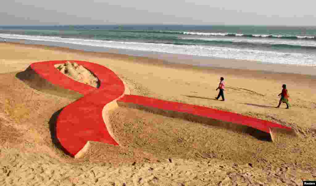 People walk near a red ribbon sand sculpture created by Indian sand artist Sudarshan Patnaik on a beach in the eastern Indian state of Odisha, November 30, 2012.