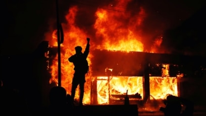 Một người biểu tình vung tay trước những tòa nhà đang bốc cháy trong các cuộc biểu tình liên quan đến cái chết của George Floyd ở Minneapolis, bang Minnesota, ngày 30 tháng 5, 2020. 