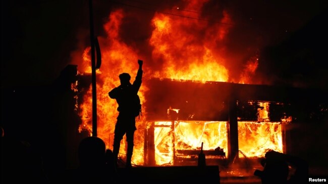 Một người biểu tình vung tay trước những tòa nhà đang bốc cháy trong các cuộc biểu tình liên quan đến cái chết của George Floyd ở Minneapolis, bang Minnesota, ngày 30 tháng 5, 2020. 